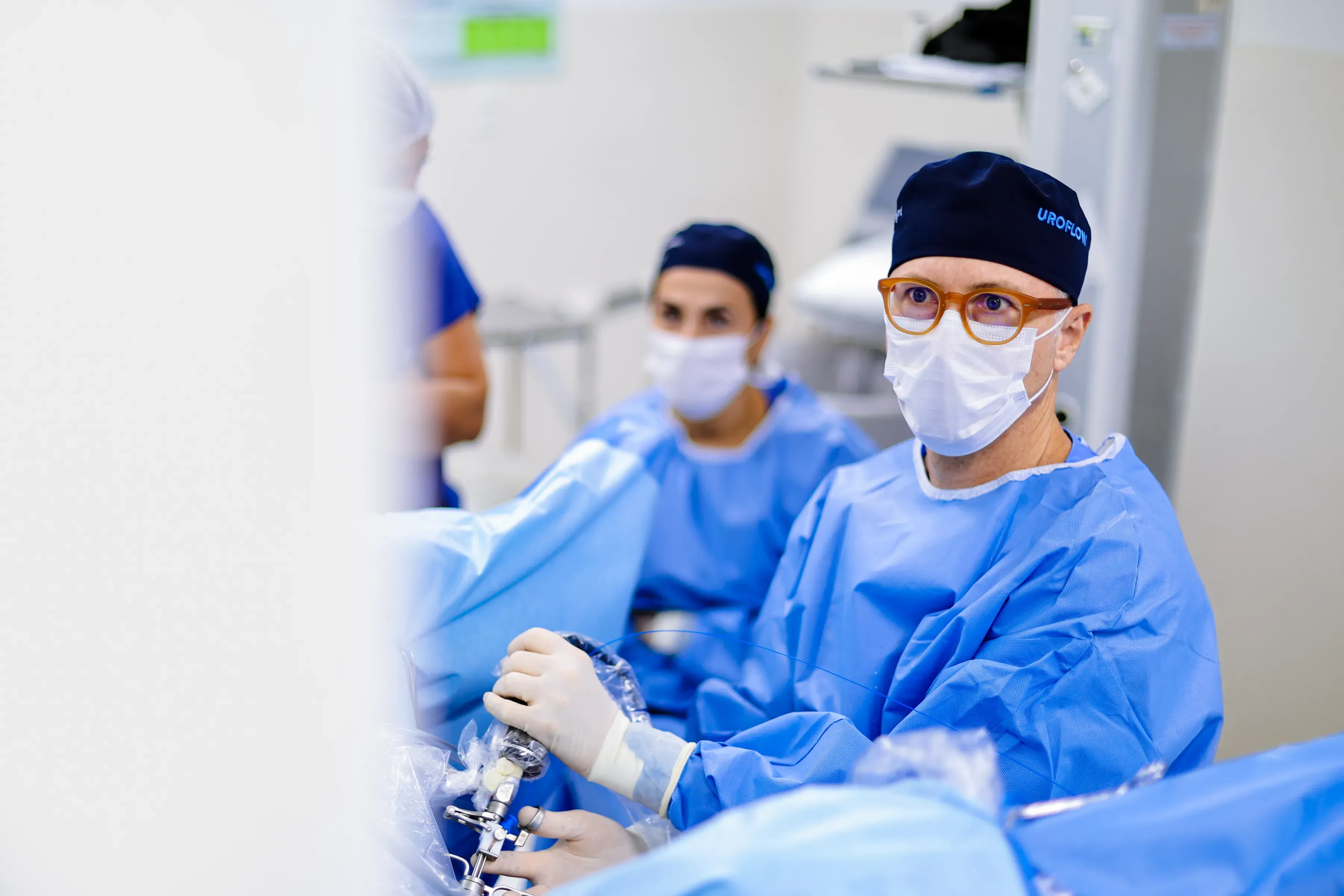 Dr. Alberto Ambrogini em centro cirúrgico, de avental, gorro e máscara, com o instrumento na mão.